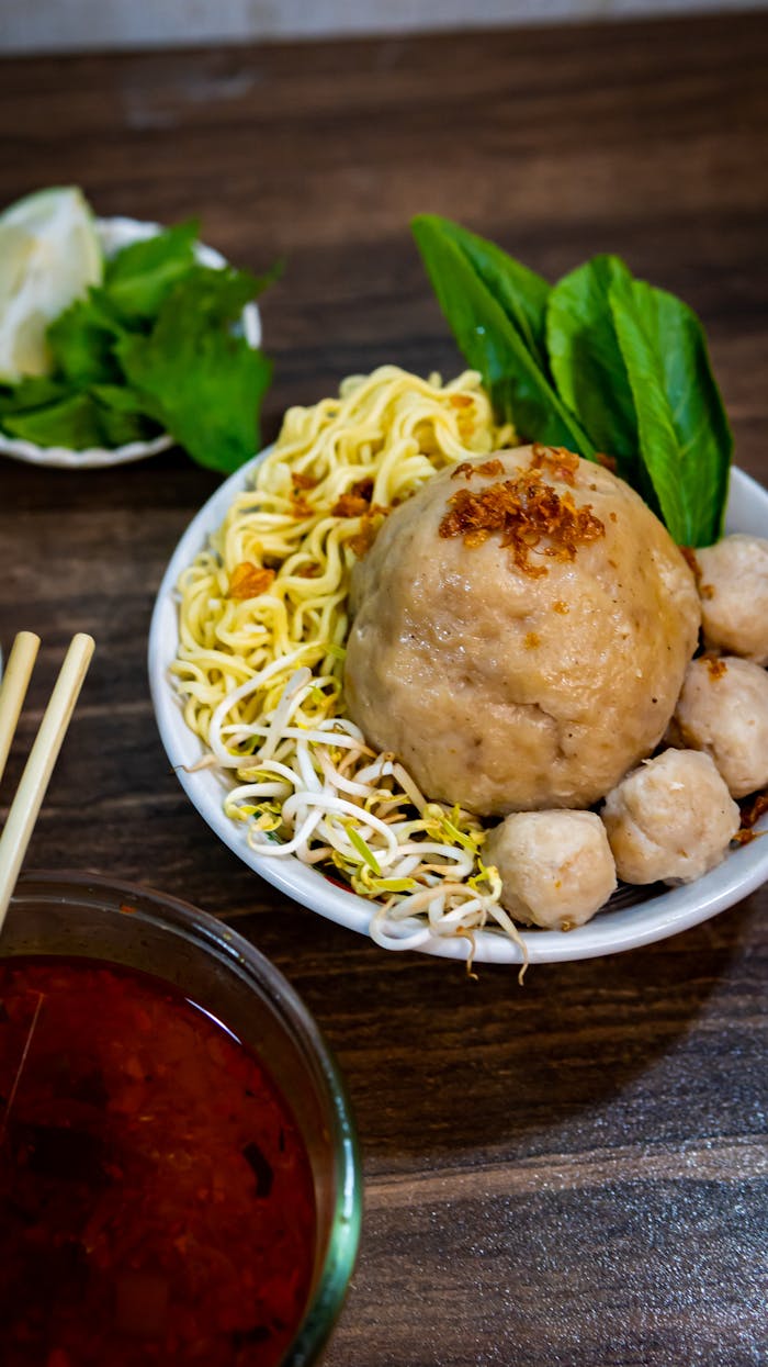 team-04 Delicious Indonesian bakso meatball dish with noodles, vegetables, and spicy sauce.