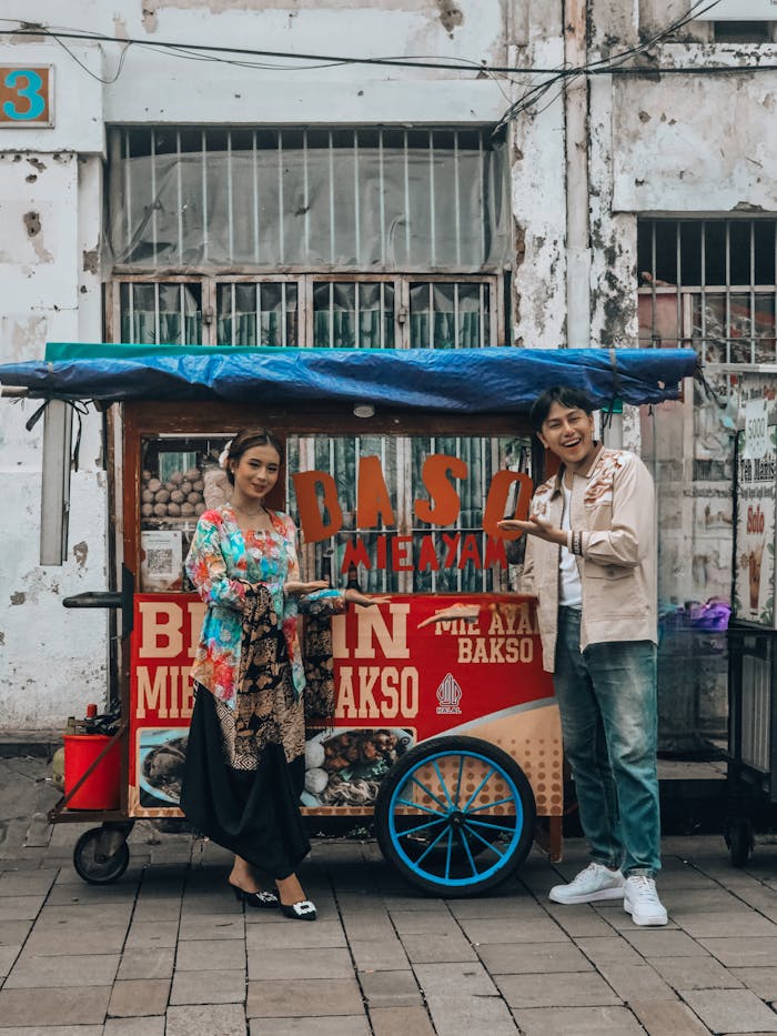 team-02 Indonesian street food cart with two happy adults enjoying bakso in Jakarta, Indonesia.